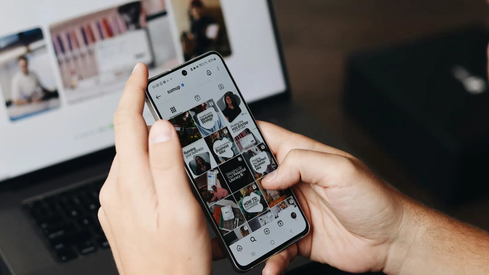 Pessoa navegando por conteúdo visual em um smartphone ao lado do computador