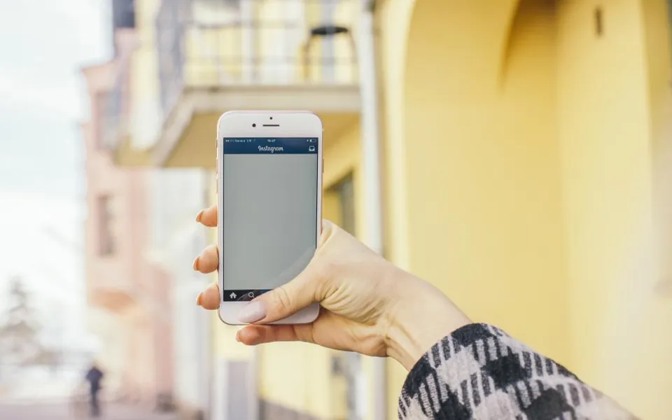 Mão segurando um celular com o aplicativo do Instagram aberto em uma rua