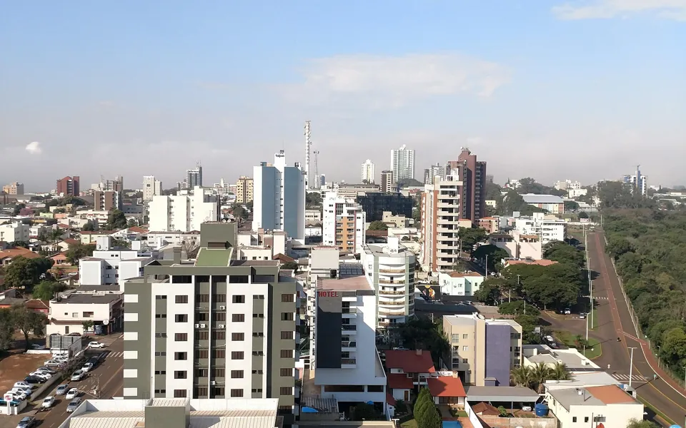 Vista do alto do centro de Toledo, no Paraná, com prédios residenciais, avenida arborizada e céu azul