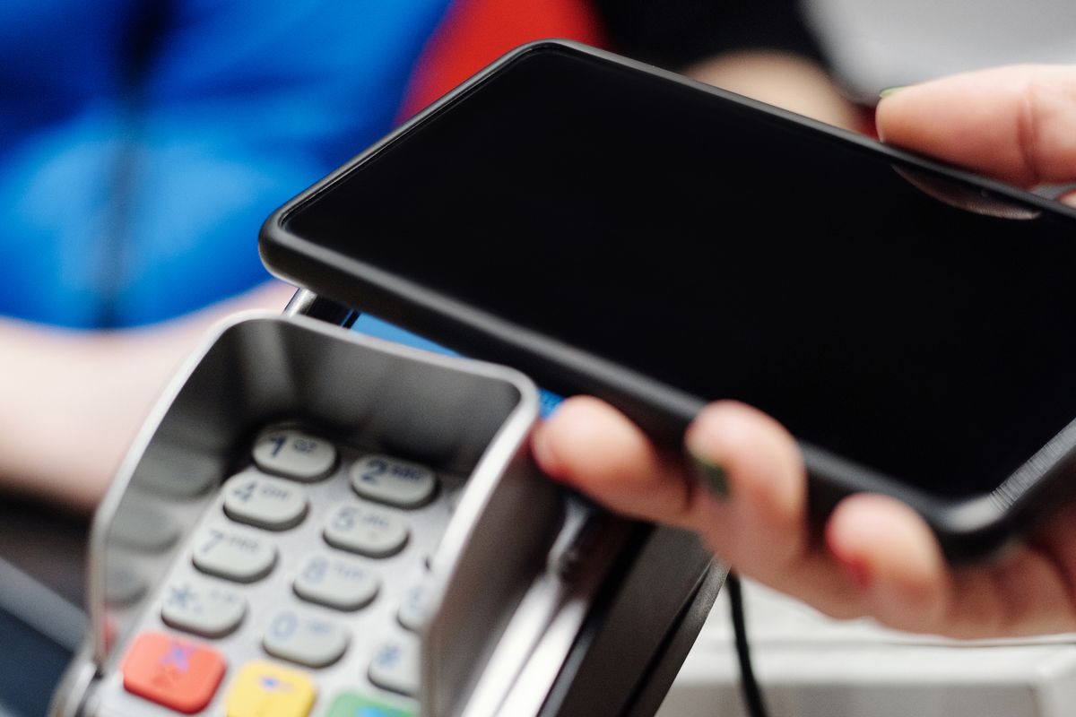 Mão aproximando um celular de uma maquininha de pagamento