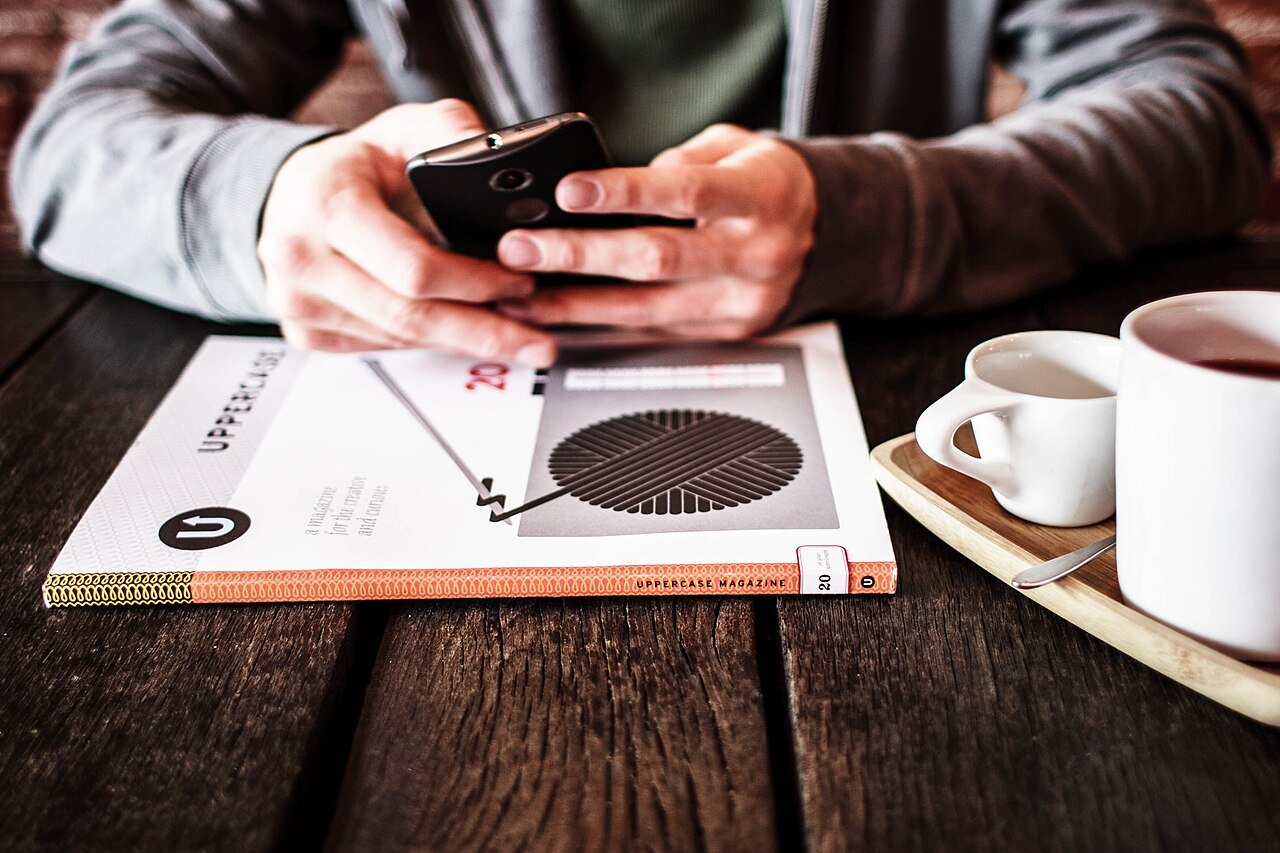 Pessoa olhando o celular em uma mesa com xícaras de café